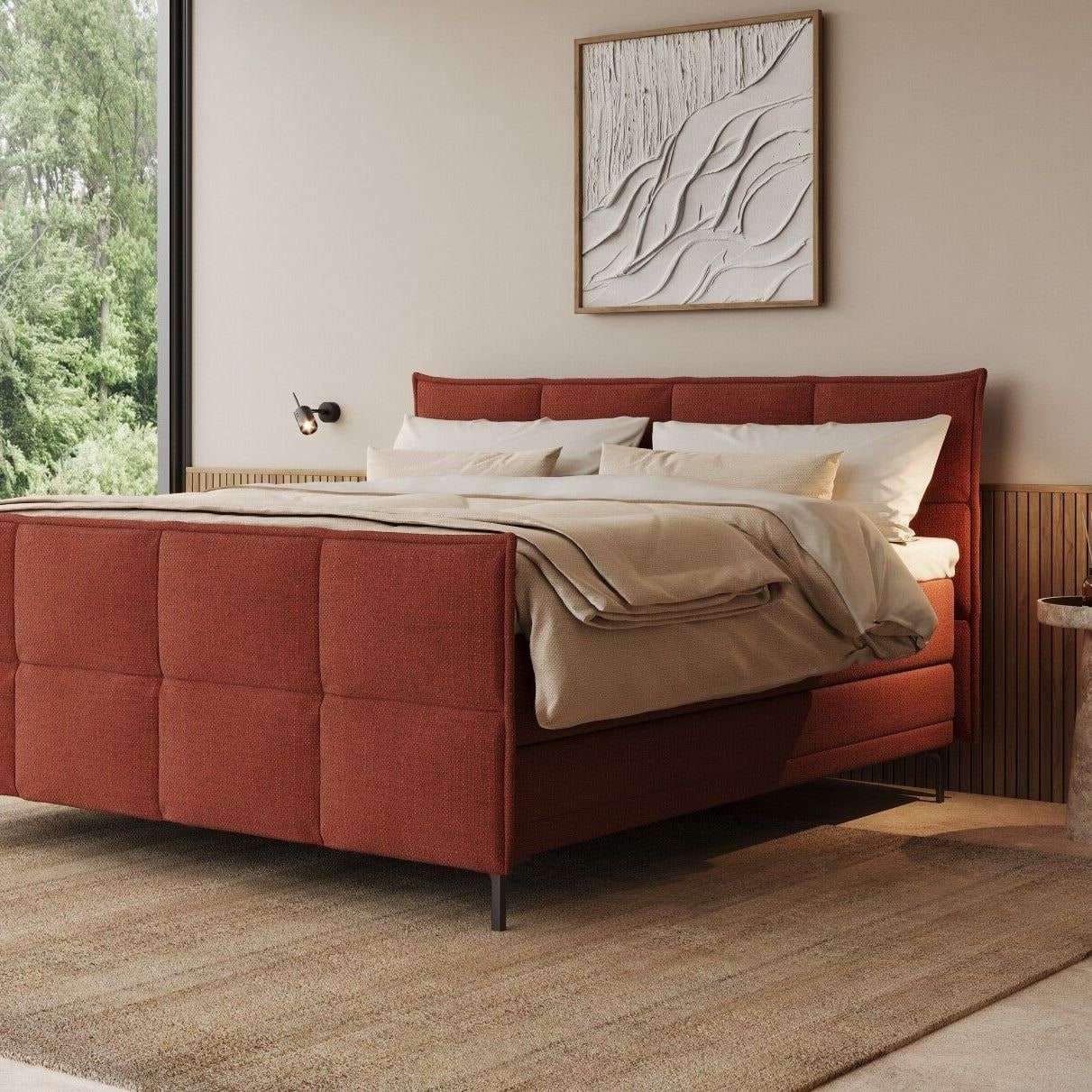 Een gestoffeerde boxspring in terracotta met hoofd- en voetbord, voor een glaswand naar de tuin