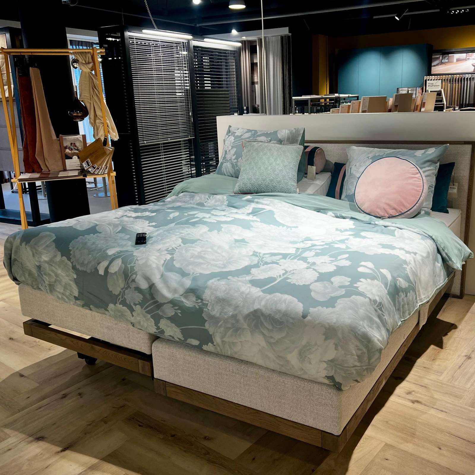 Een hoog-laag boxspring in de showroom, met een lichtgroen dekbed met bloemen en de afstandsbediening op het bed